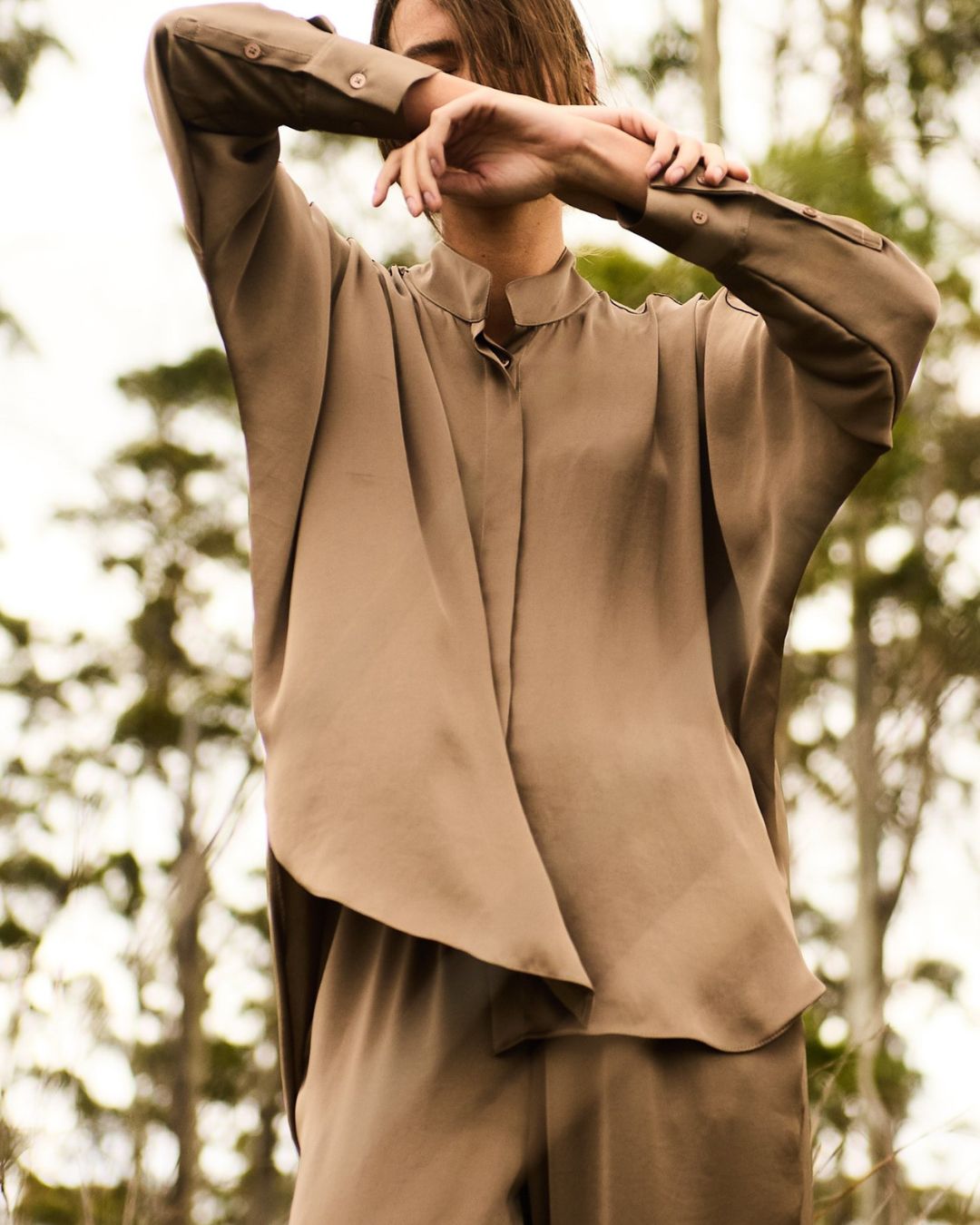 Person wearing a beige shirt and pants with a blurred natural background